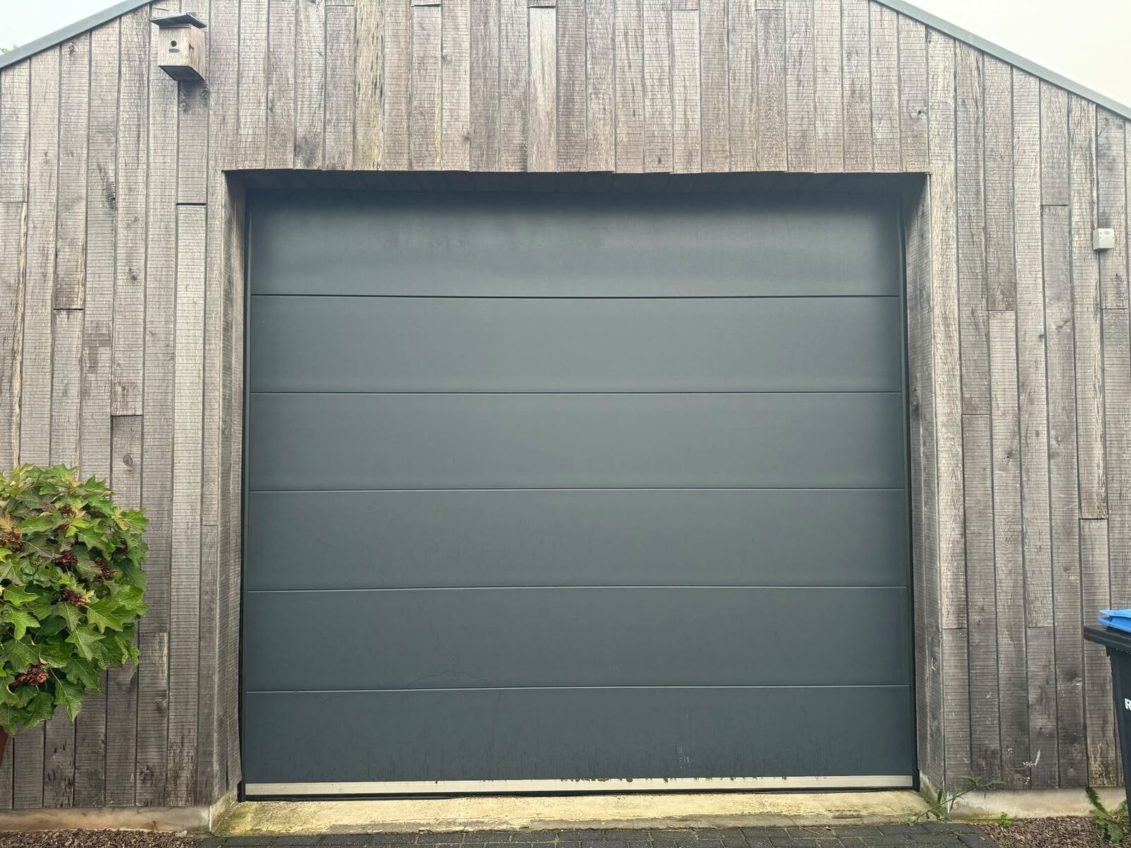 Grote antracietkleurige garagedeur in houten schuur